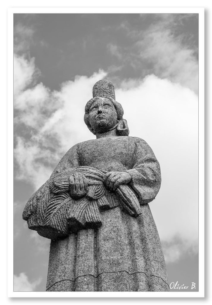 Statue en granit d&#039;un Bigouden en contre-plongée, défiant le ciel nuageux