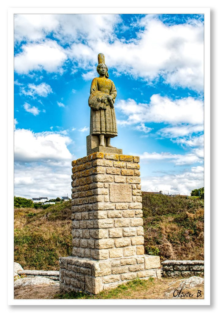 Statue Bigouden en granit surplombant le port de Pors-Poullan, face à l&#039;océan sous un ciel bleu