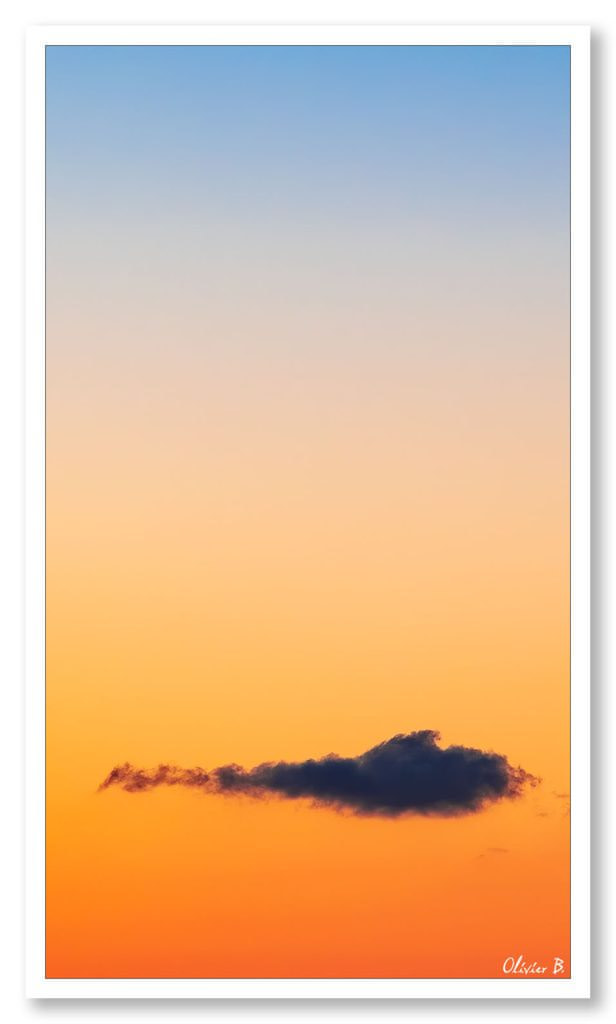 Nuage solitaire dans un ciel dégradé bleu-rouge lors d&#039;un magnifique coucher de soleil